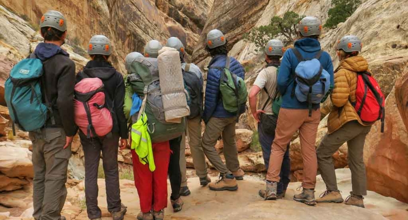 A group of students wearing helmets face away from the camera looking into a canyon